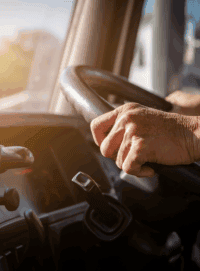 Older person's hands gripping the steering wheel of a big rig