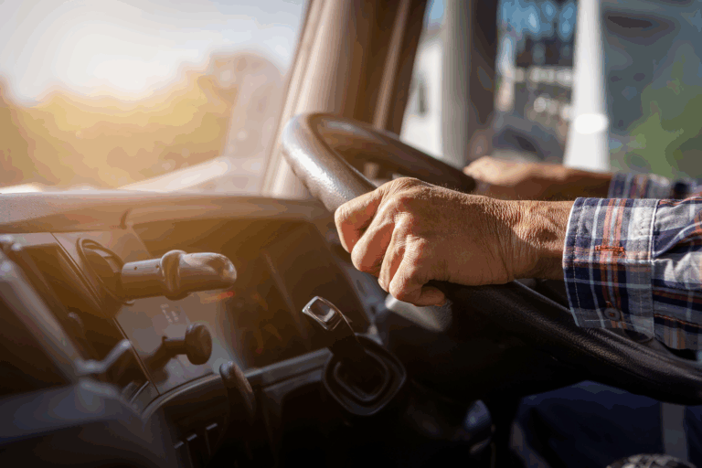 Older person's hands gripping the steering wheel of a big rig