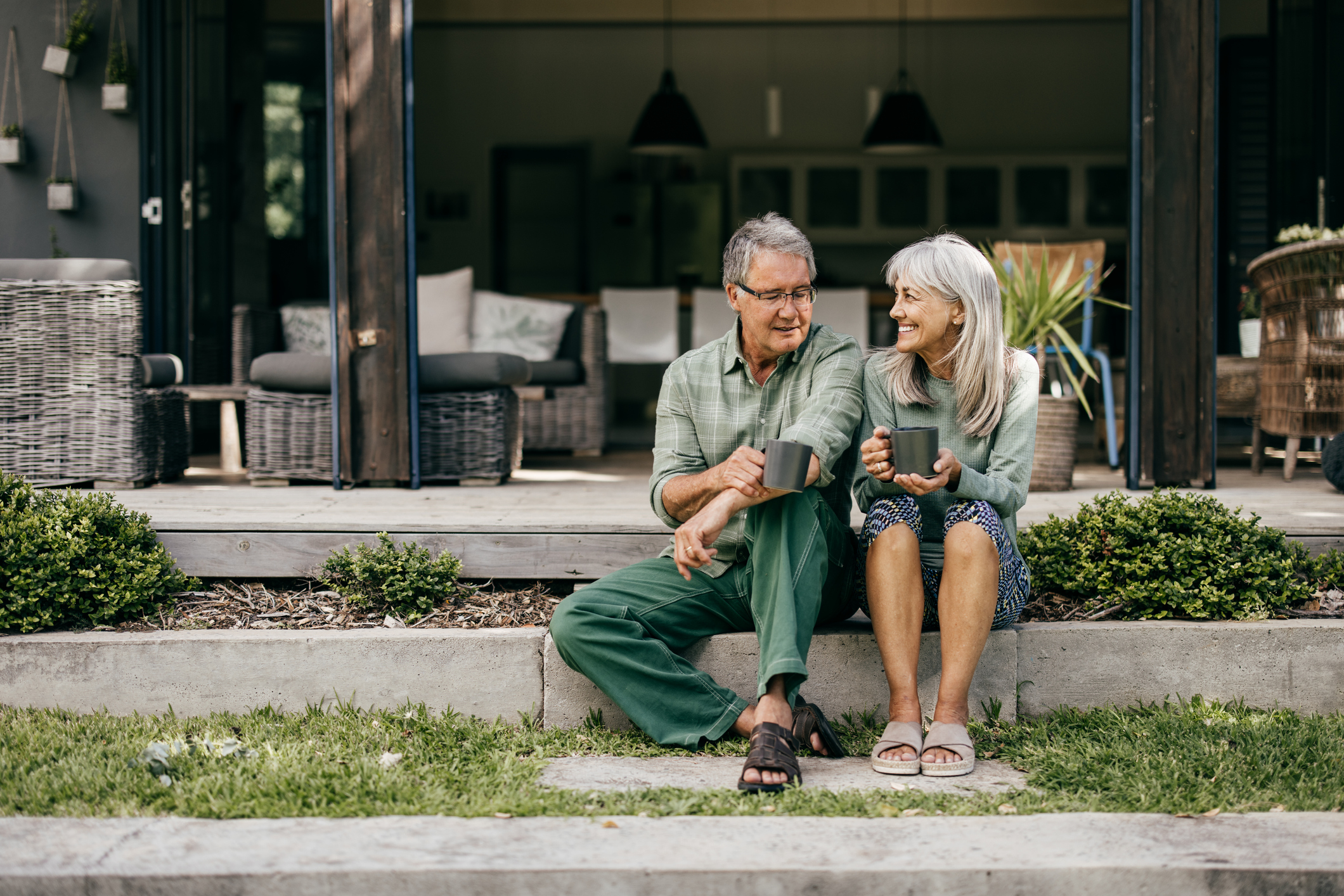 With coffee in hand, a senior couple in their 60s embraces a quiet moment, appreciating the beauty of their home.