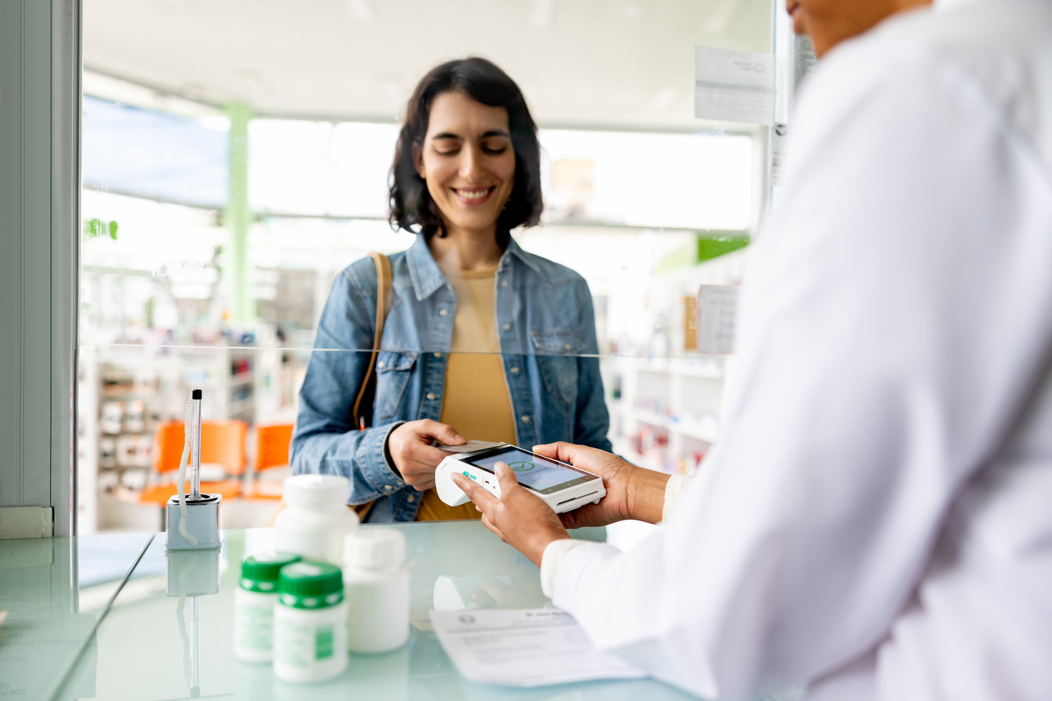 Happy Latin American woman paying by card while buying medicines at the pharmacy - tap to pay concepts