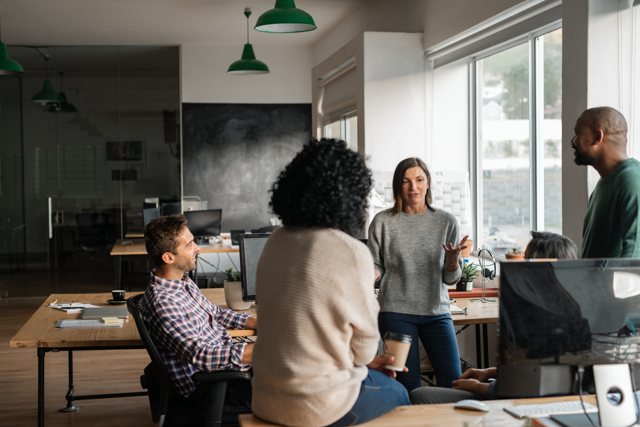 Smiling group of diverse designers discussing business together while having a casual meeting around their desks in their startup office