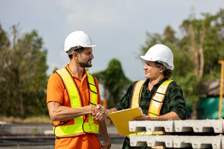 two men in hard hats and high-vis vests performing a handshake