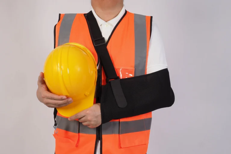 person in high visibility vest with arm in a sling holding a hard hat